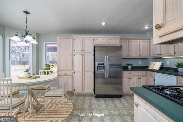 kitchen with stovetop, white dishwasher, dark countertops, a notable chandelier, and stainless steel fridge