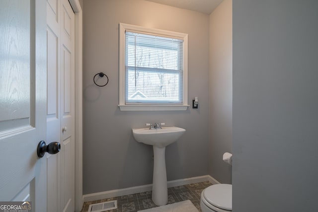 half bathroom featuring visible vents, toilet, baseboards, and a sink