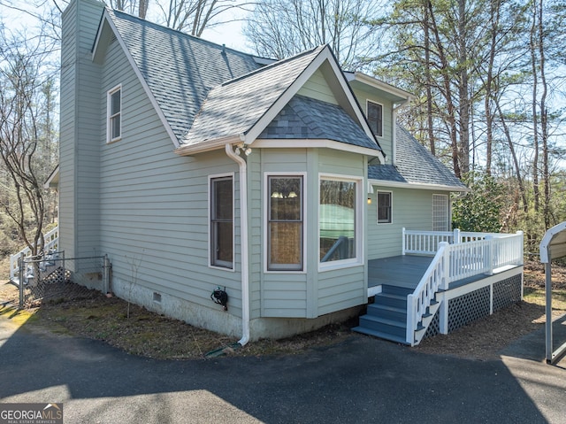 exterior space featuring crawl space, a chimney, a wooden deck, and roof with shingles