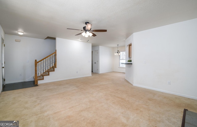 unfurnished living room featuring baseboards, stairway, light carpet, ceiling fan with notable chandelier, and a textured ceiling