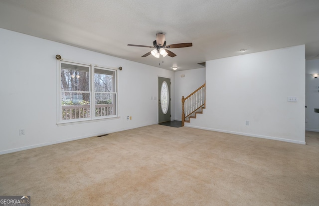 unfurnished living room featuring visible vents, a ceiling fan, a textured ceiling, carpet floors, and stairs