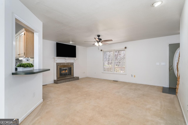 unfurnished living room with visible vents, light carpet, a glass covered fireplace, and a ceiling fan