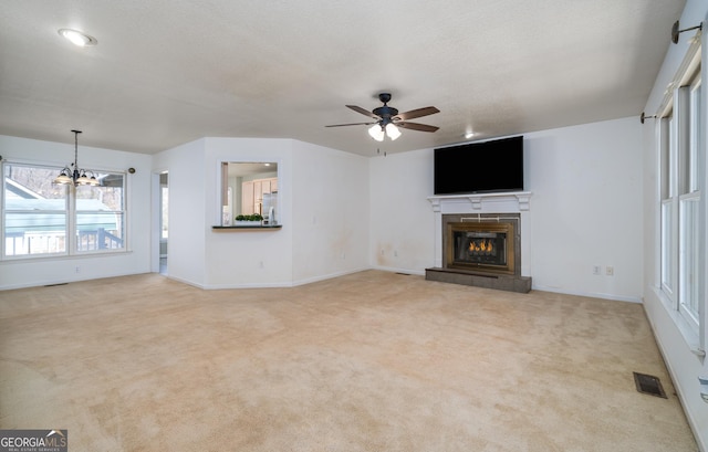 unfurnished living room featuring visible vents, ceiling fan with notable chandelier, a glass covered fireplace, carpet flooring, and baseboards