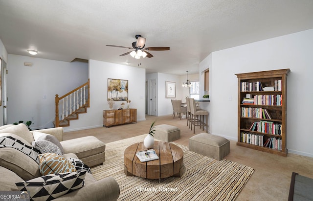 living area with baseboards, stairway, carpet floors, ceiling fan with notable chandelier, and a textured ceiling