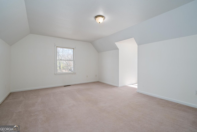 additional living space with baseboards, lofted ceiling, and light colored carpet