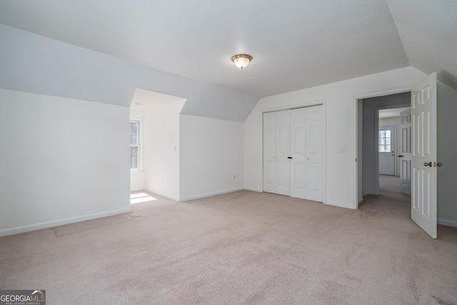 additional living space featuring baseboards, light colored carpet, and vaulted ceiling