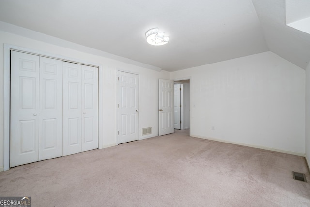 unfurnished bedroom with carpet, visible vents, baseboards, vaulted ceiling, and two closets