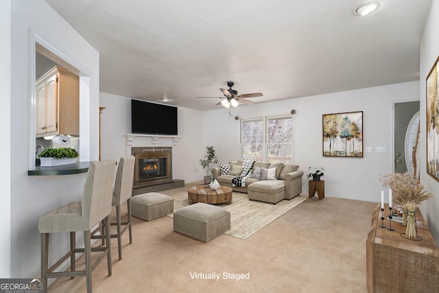 living room featuring a glass covered fireplace, light colored carpet, baseboards, and a ceiling fan