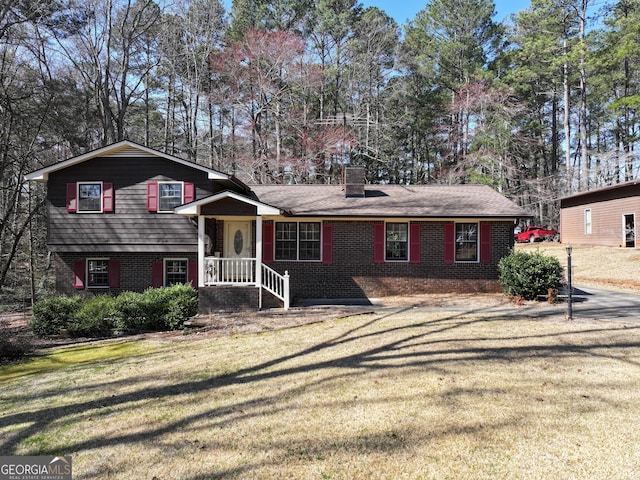 tri-level home with brick siding, a chimney, and a front yard