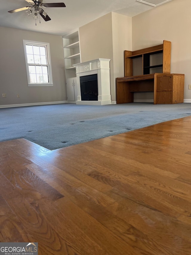 unfurnished living room featuring wood finished floors, a ceiling fan, baseboards, and a fireplace with raised hearth