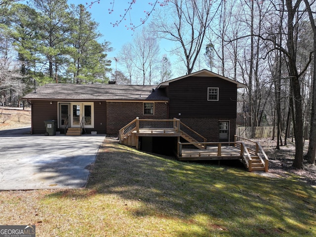 back of house featuring driveway, entry steps, a yard, a wooden deck, and brick siding