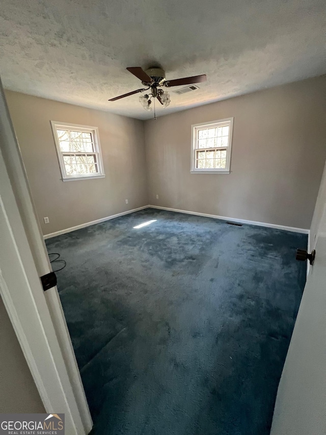 spare room featuring dark colored carpet, visible vents, a healthy amount of sunlight, and a ceiling fan