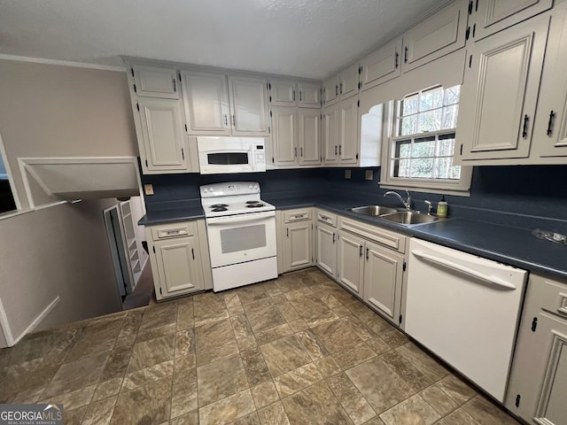 kitchen with dark countertops, ornamental molding, white appliances, and a sink