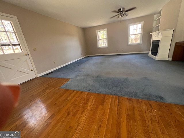 unfurnished living room with dark wood finished floors, a glass covered fireplace, baseboards, and ceiling fan