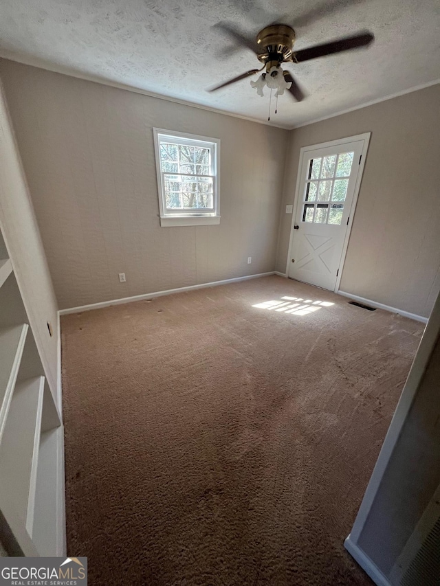 carpeted spare room with a wealth of natural light, visible vents, a textured ceiling, and ceiling fan