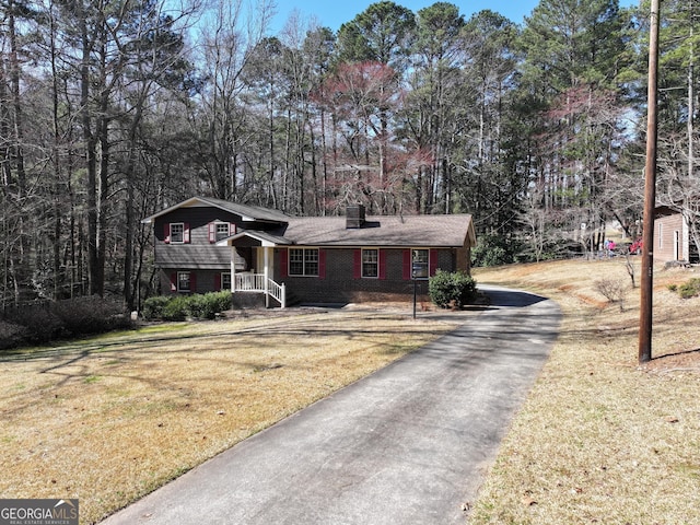 tri-level home with aphalt driveway, brick siding, and a front lawn