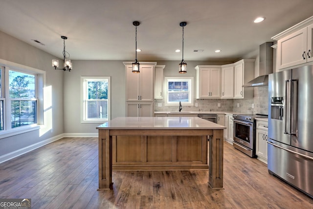 kitchen featuring stainless steel appliances, white cabinets, a center island, and wall chimney range hood