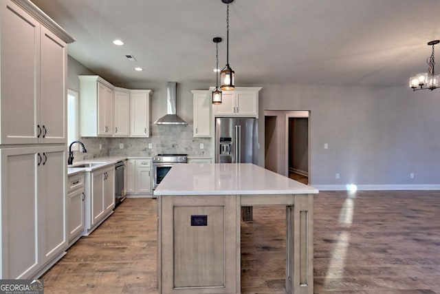 kitchen with tasteful backsplash, wall chimney range hood, wood finished floors, stainless steel appliances, and a sink