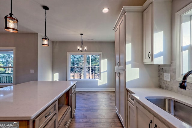 kitchen featuring backsplash, a center island, light stone countertops, dark wood-style floors, and a sink