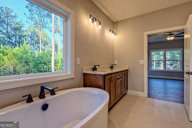 full bath featuring a freestanding tub, a sink, tile patterned flooring, double vanity, and baseboards