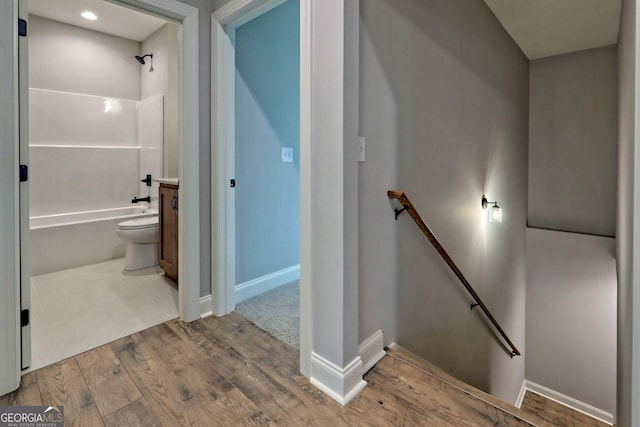 interior space with vanity, wood finished floors, baseboards,  shower combination, and toilet