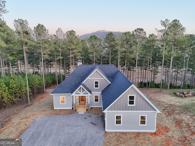 chalet / cabin featuring board and batten siding, a chimney, gravel driveway, and roof with shingles