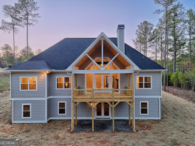 rear view of house with a shingled roof, a deck, and a chimney