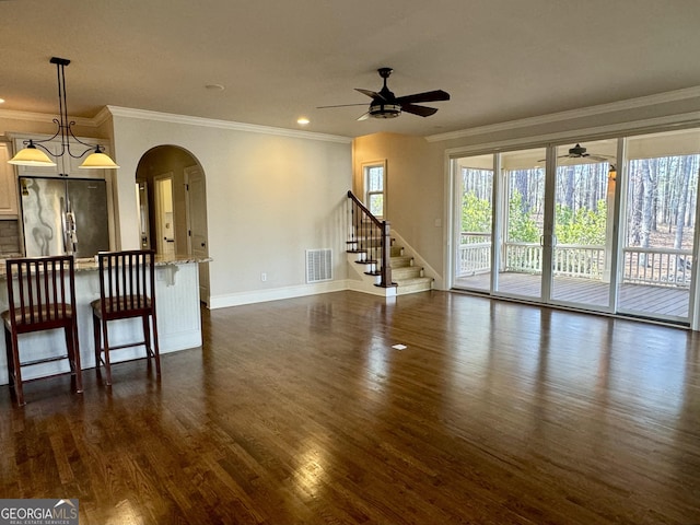 unfurnished living room with visible vents, arched walkways, dark wood-style floors, and ceiling fan
