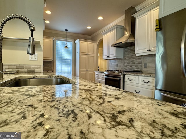 kitchen featuring a sink, stainless steel appliances, light stone counters, and wall chimney exhaust hood