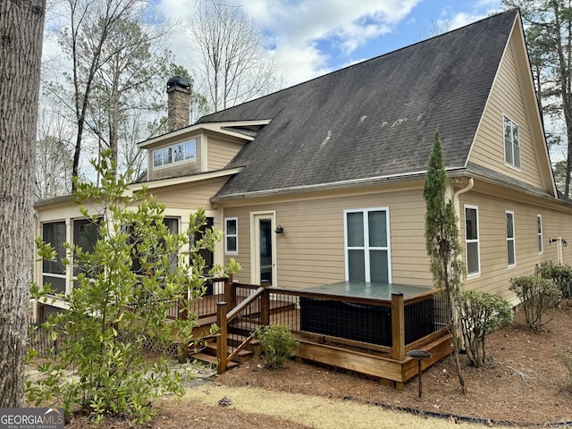 back of property with a chimney, a shingled roof, and a deck