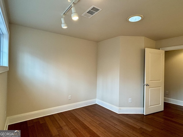 empty room with baseboards, visible vents, wood finished floors, and track lighting