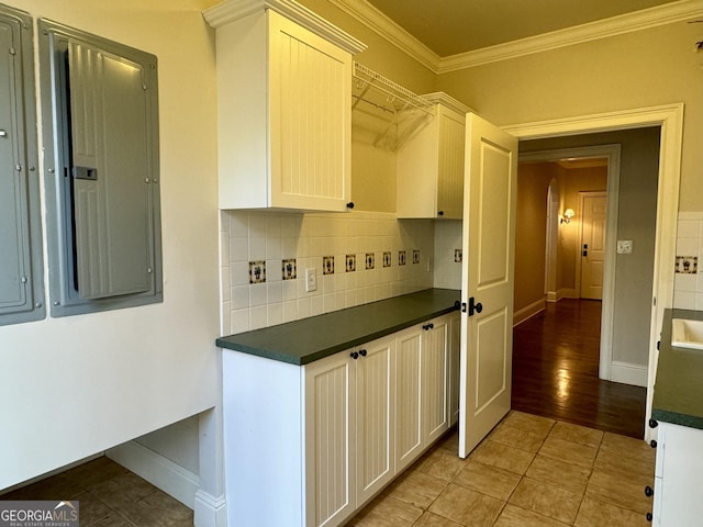 kitchen with electric panel, crown molding, baseboards, dark countertops, and backsplash