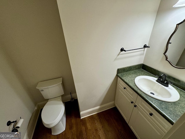 half bathroom with toilet, vanity, baseboards, and wood finished floors