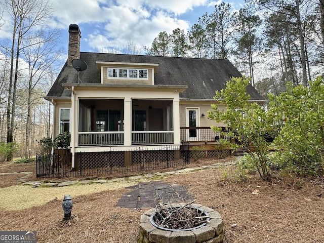 rear view of property with a fire pit, a chimney, a wooden deck, a shingled roof, and a sunroom
