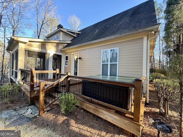 rear view of house with a shingled roof, a deck, and a chimney