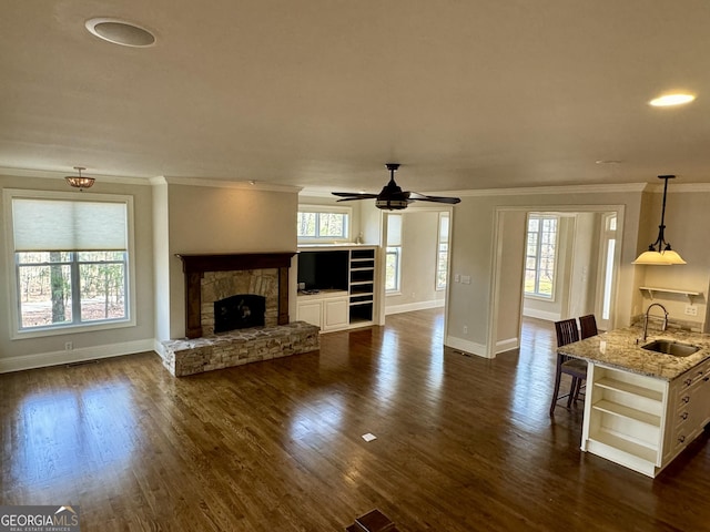 unfurnished living room featuring baseboards, a fireplace, ornamental molding, dark wood-type flooring, and a sink