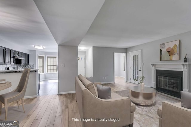 living area with a glass covered fireplace, baseboards, and light wood-style floors