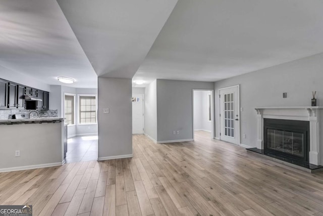 unfurnished living room featuring light wood finished floors, a glass covered fireplace, and baseboards