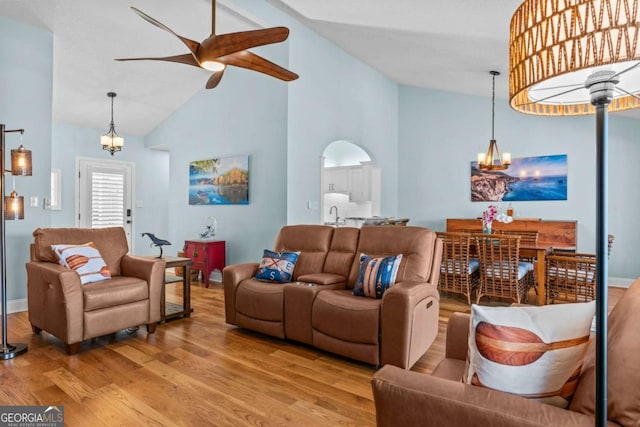 living room with ceiling fan with notable chandelier, high vaulted ceiling, baseboards, and wood finished floors