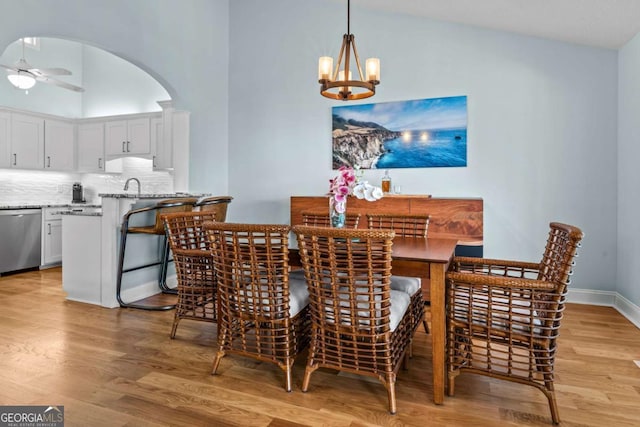 dining area featuring high vaulted ceiling, ceiling fan with notable chandelier, light wood-style floors, and arched walkways