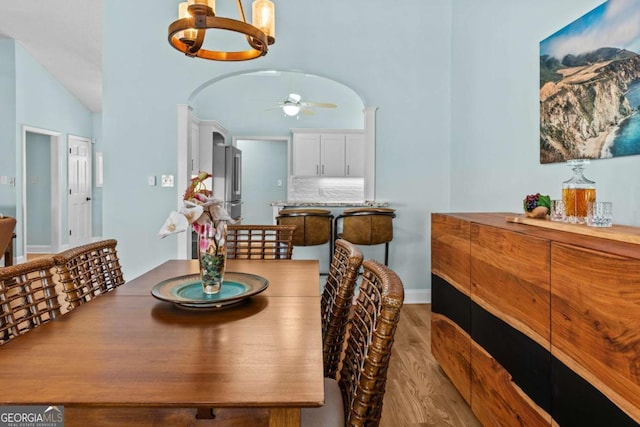 dining room with baseboards, lofted ceiling, ceiling fan with notable chandelier, wood finished floors, and arched walkways