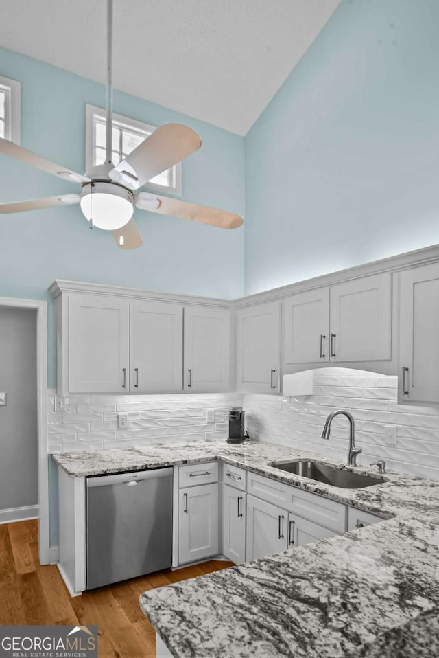 kitchen with high vaulted ceiling, a sink, stainless steel dishwasher, light stone countertops, and ceiling fan