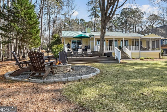 back of house featuring a fire pit, a chimney, metal roof, a yard, and a standing seam roof