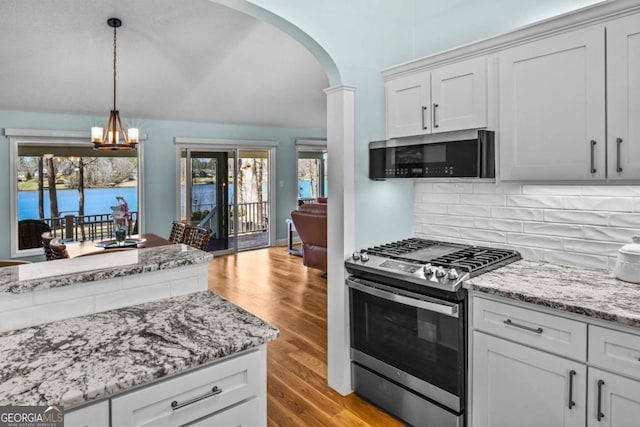 kitchen with light wood-style flooring, arched walkways, stainless steel appliances, a notable chandelier, and backsplash