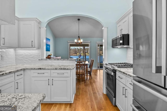 kitchen featuring arched walkways, a notable chandelier, appliances with stainless steel finishes, and white cabinets