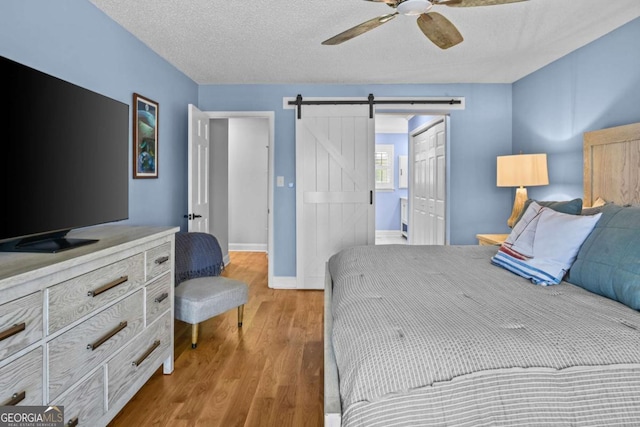 bedroom featuring a barn door, wood finished floors, baseboards, and a textured ceiling