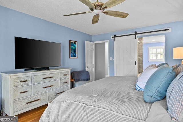 bedroom featuring a ceiling fan, a barn door, wood finished floors, and a textured ceiling