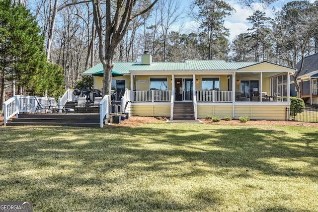 back of property featuring a lawn, a standing seam roof, a sunroom, metal roof, and a chimney