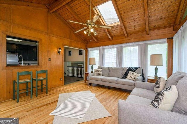 living room featuring wood finished floors, vaulted ceiling with skylight, wooden walls, wooden ceiling, and ceiling fan
