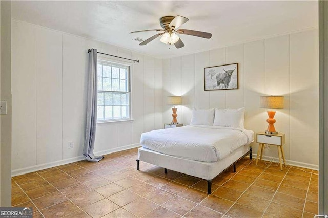 bedroom with tile patterned floors, a decorative wall, baseboards, and ceiling fan